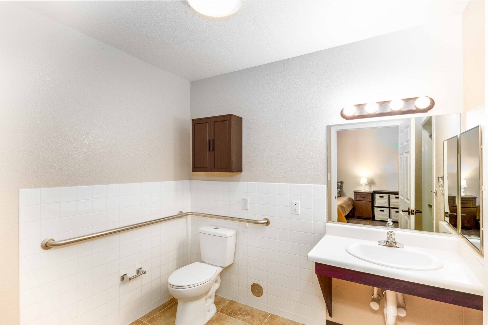 Sink and toilet beneath a wall cabinet beside grab bars.