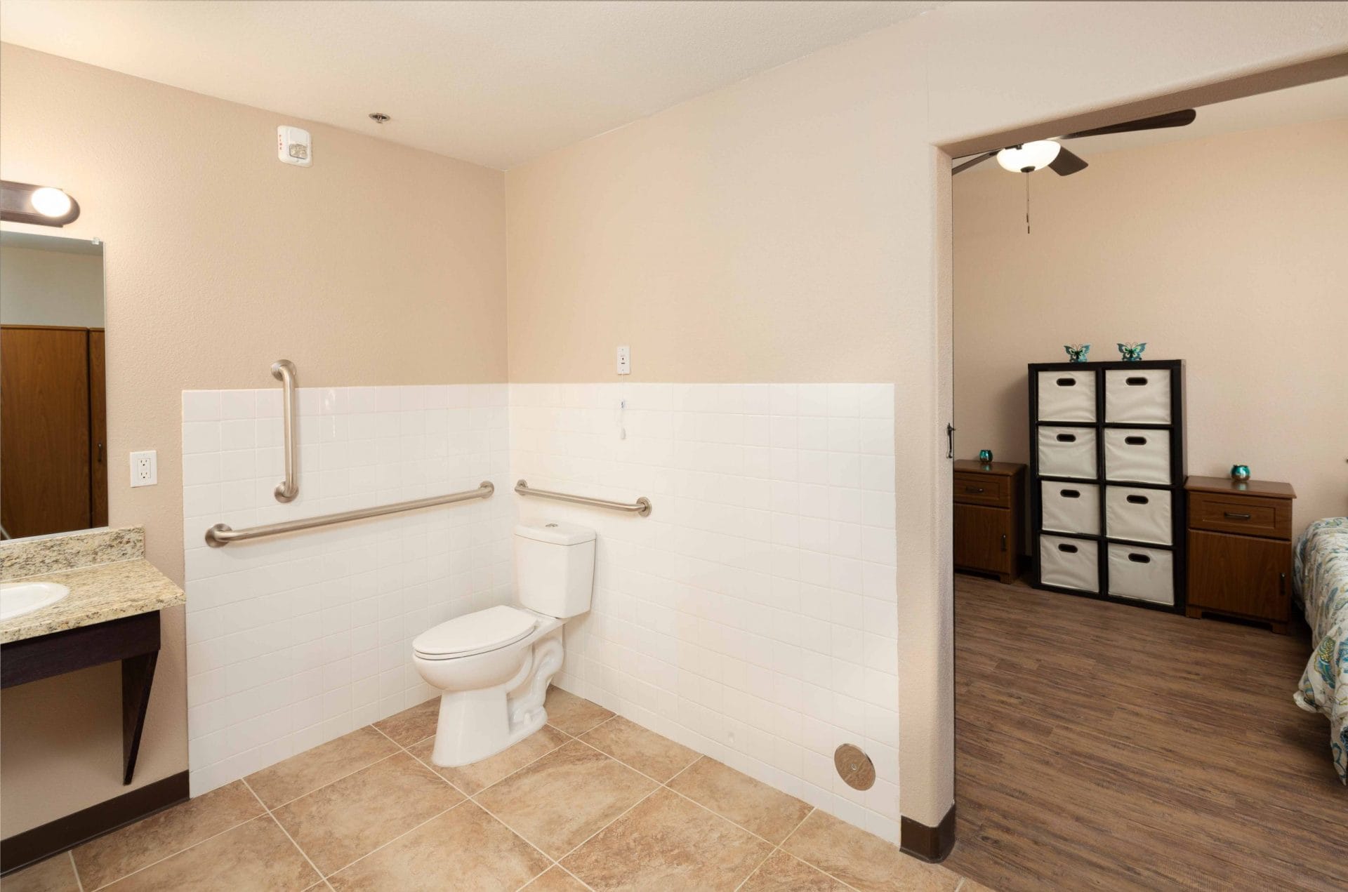 Bathroom with grab bars and a wide opening toward a bedroom.